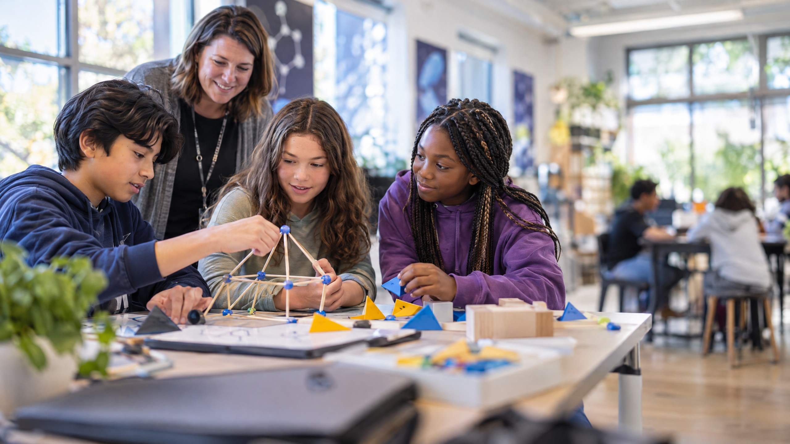 Middle-school students collaborate on a hands-on problem while a teacher coaches nearby.